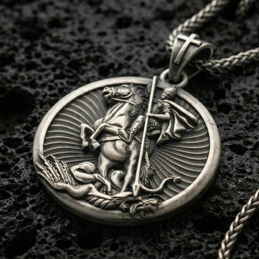 Oxidized Saint George pendant with mounted warrior relief, spear detail, and round medallion design displayed on dark volcanic rock in a close-up luxury jewelry composition