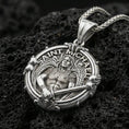 Load image into Gallery viewer, Polished silver Archangel Michael medallion with round frame, armored angel relief, and decorative gothic border placed on textured volcanic rock in a premium studio product shot
