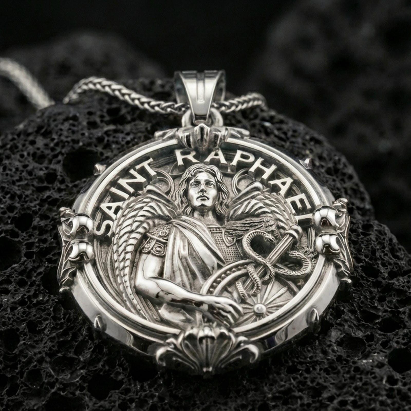 Polished silver Archangel Raphael medallion with round ornamental frame, detailed angel relief, and sacred healing symbol placed on textured volcanic rock in a premium studio product shot