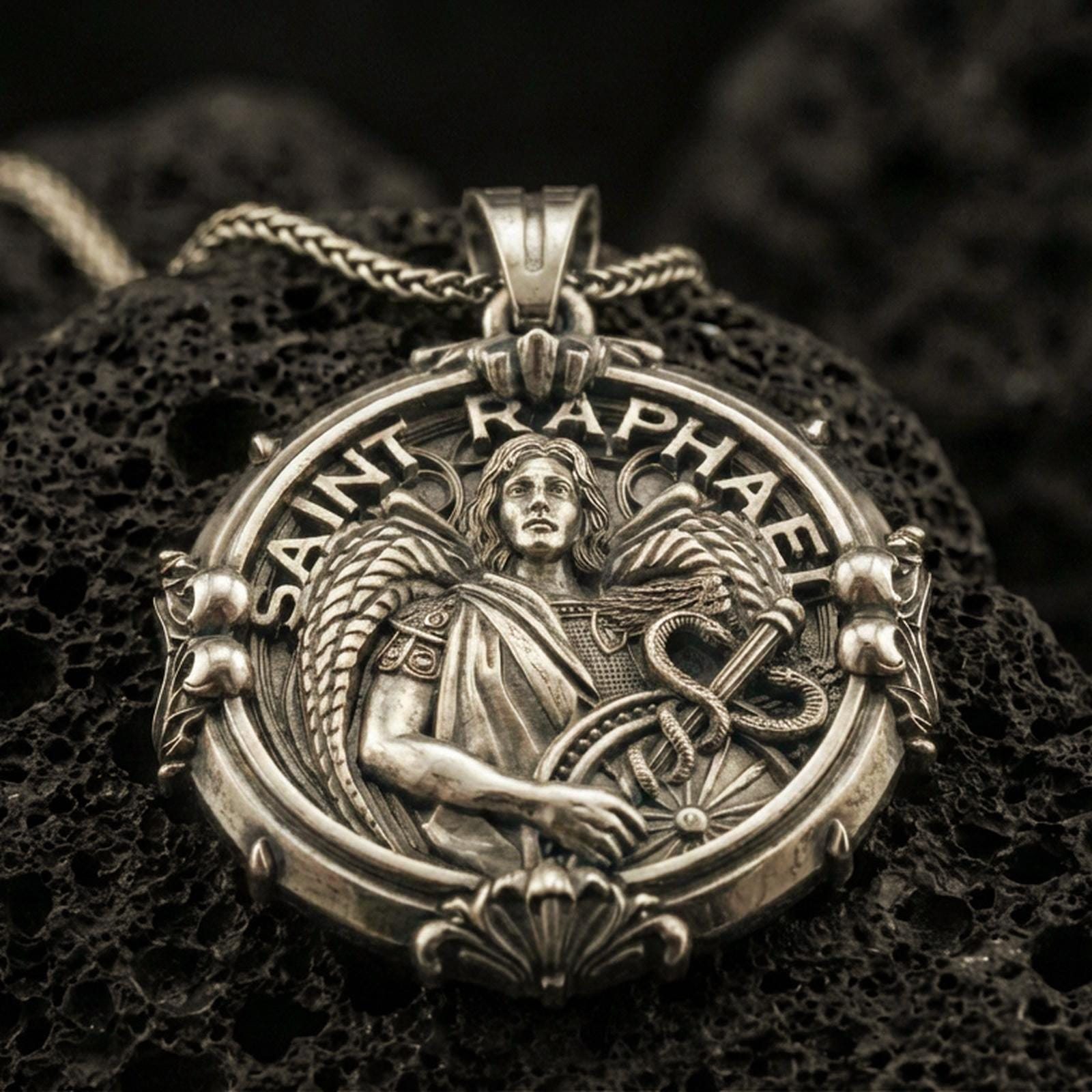Bronze Saint Raphael pendant with winged archangel figure, healing staff with serpent, and Saint Raphael inscription displayed on dark volcanic rock in a close-up luxury jewelry composition