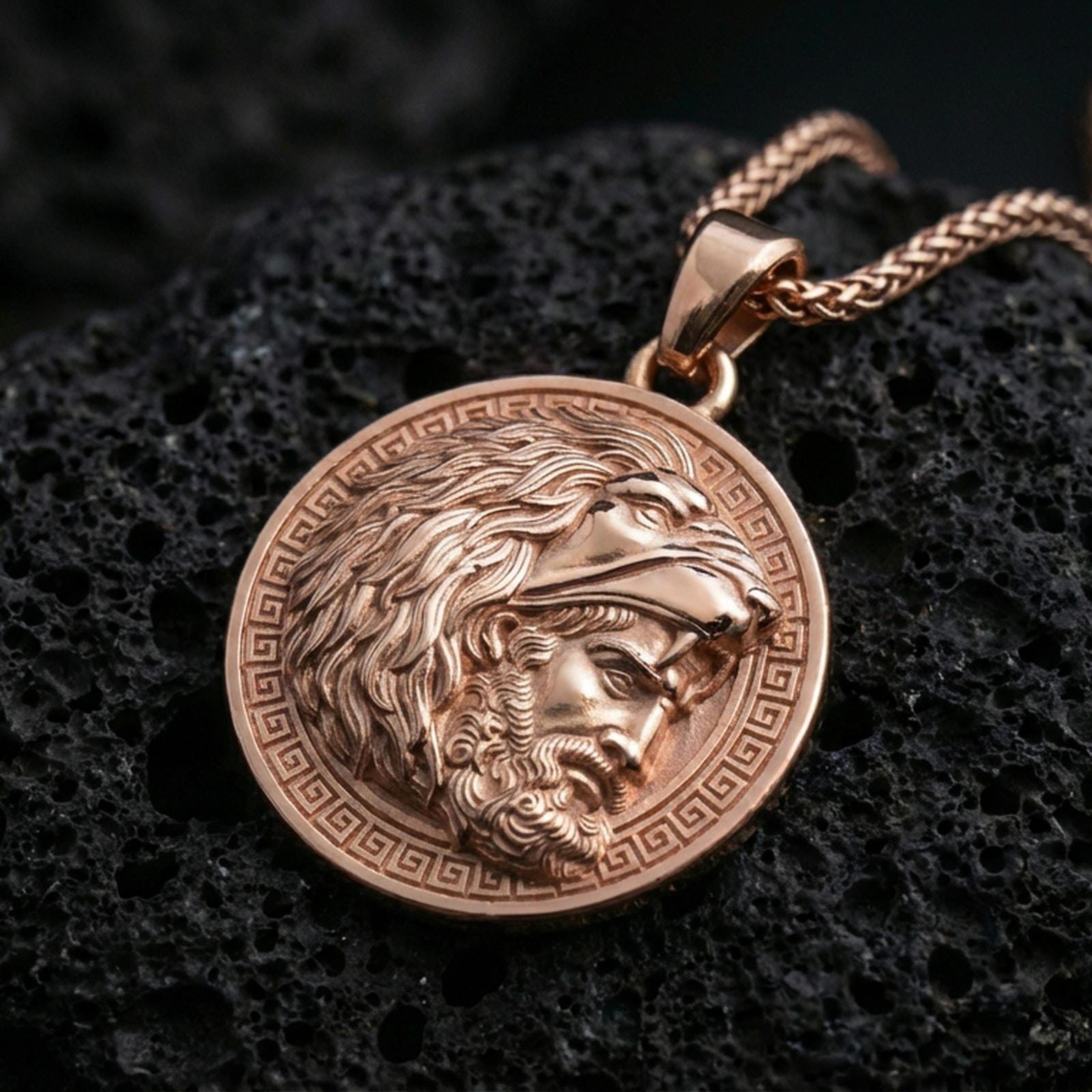 Rose gold plated Heracles lion helmet coin pendant necklace on textured volcanic rock, centered studio-style close-up showcasing soft rosy glow and intricate Greek mythology portrait detailing.