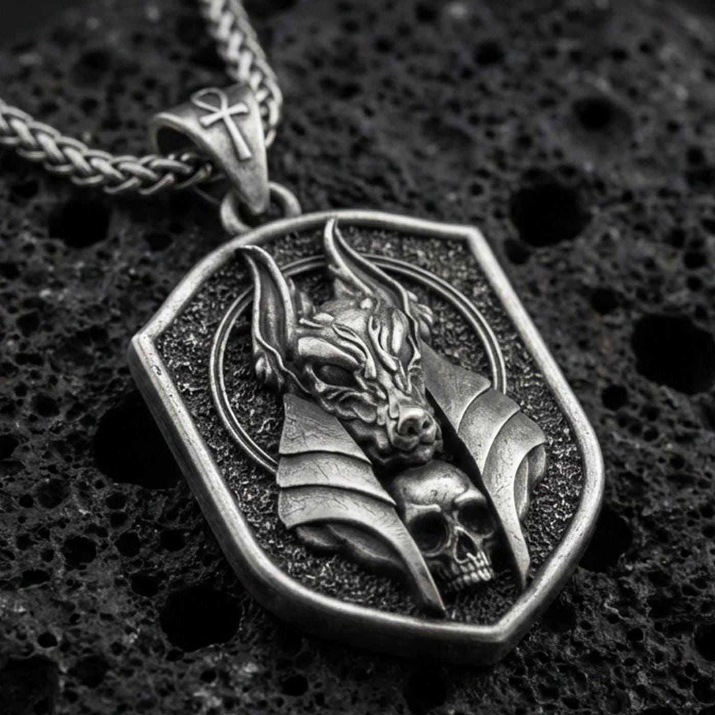 Oxidized Anubis pendant necklace on textured volcanic rock, centered close-up highlighting the jackal god head, halo-like frame, skull detail, and deep antique shadowed contrast.
