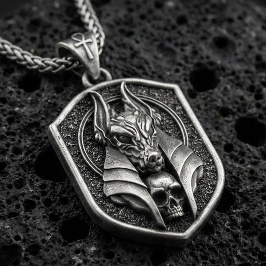 Oxidized Anubis pendant necklace on textured volcanic rock, centered close-up highlighting the jackal god head, halo-like frame, skull detail, and deep antique shadowed contrast.