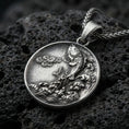 Load image into Gallery viewer, Oxidized koi fish medallion pendant necklace on textured volcanic rock, centered close-up highlighting the leaping koi, wave relief, and deep antique shadowed contrast on the smooth coin background.
