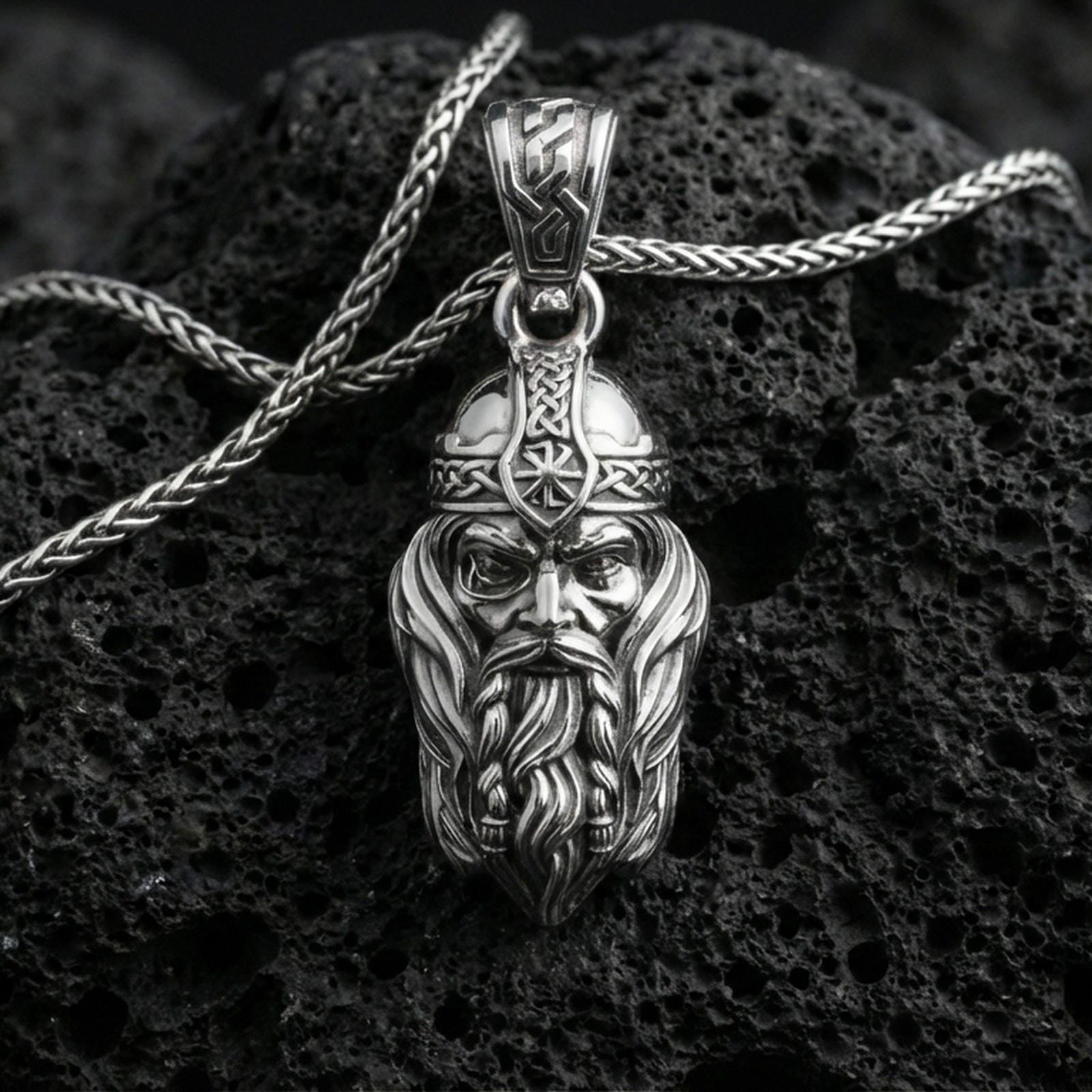 Polished silver Viking warrior head pendant necklace on textured volcanic rock, crisp macro product photo emphasizing clean edges, sharp facial sculpting, and bright reflective highlights on the helmet and beard.