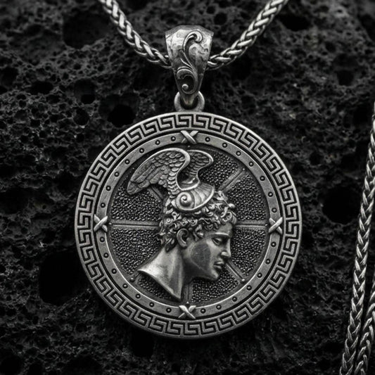Oxidized Perseus coin pendant necklace on textured volcanic rock, centered close-up highlighting the Greek key border, winged helmet profile, and deep antique shadowed contrast.
