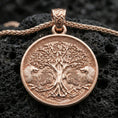 Load image into Gallery viewer, Rose gold plated Yggdrasil tree of life pendant necklace on textured volcanic rock, centered studio-style close-up showcasing soft rosy glow and ornate Viking knotwork detailing around the medallion.

