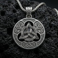 Load image into Gallery viewer, Oxidized Celtic triquetra pendant necklace on textured volcanic rock, centered close-up highlighting the raised Trinity knot, ornate scrollwork, and deep antique shadowed contrast.
