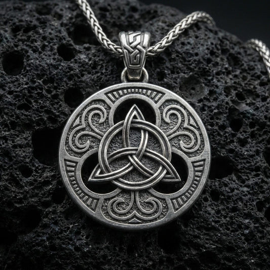 Oxidized Celtic triquetra pendant necklace on textured volcanic rock, centered close-up highlighting the raised Trinity knot, ornate scrollwork, and deep antique shadowed contrast.