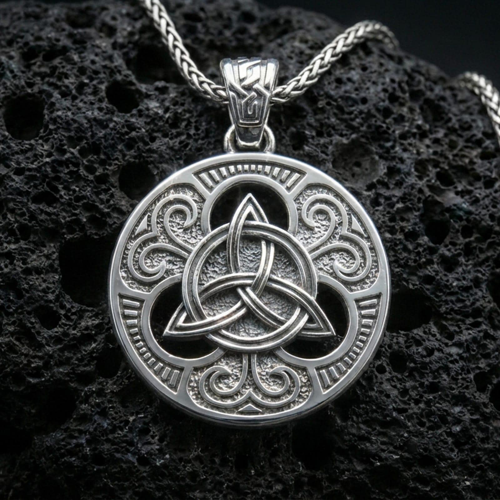 Polished silver Celtic triquetra pendant necklace on textured volcanic rock, crisp macro product photo emphasizing clean edges, sharp knotwork relief, and bright reflective highlights across the circular frame.