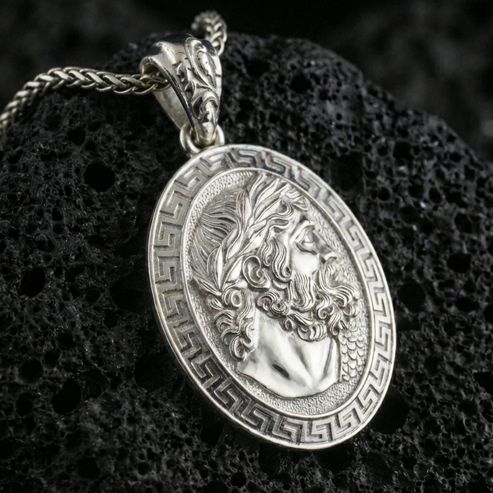 Polished silver Hades coin pendant necklace on textured volcanic rock, crisp macro product photo emphasizing clean edges, sharp beard-and-hair engraving, and bright reflective highlights on the relief.