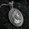Load image into Gallery viewer, Oxidized Hades coin pendant necklace on textured volcanic rock, centered close-up highlighting the Greek key border, laurel-crowned profile, and deep antique shadowed contrast.
