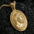 Load image into Gallery viewer, Gold plated Hades coin pendant necklace on textured volcanic rock, premium close-up with warm reflective shine across the laurel wreath, facial sculpting, and raised meander frame.
