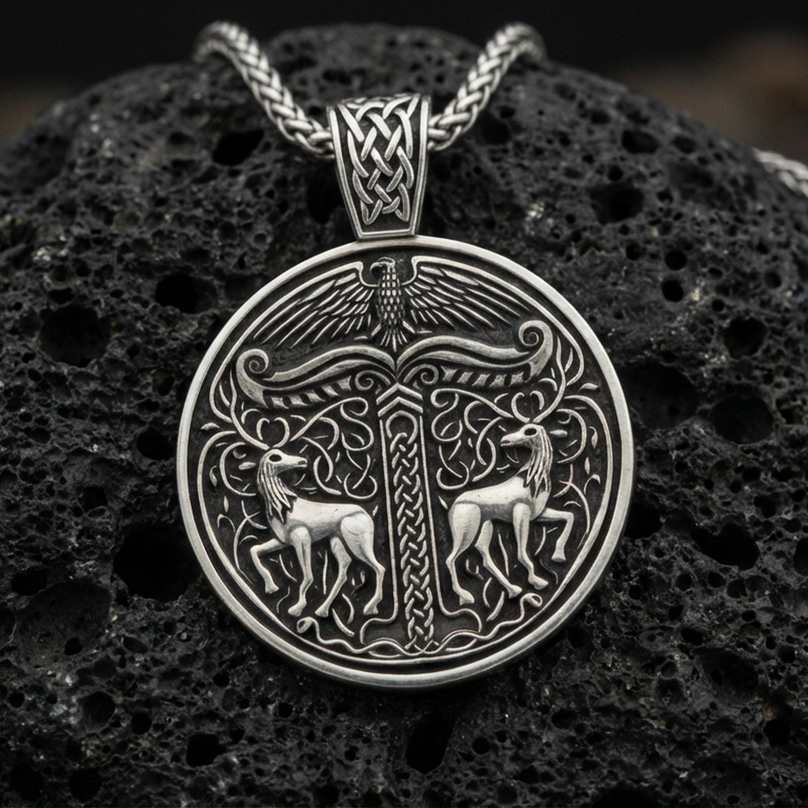 Oxidized Viking deer medallion pendant necklace on textured volcanic rock, centered close-up highlighting the twin stag motif, carved knotwork column, and deep antique shadowed contrast.