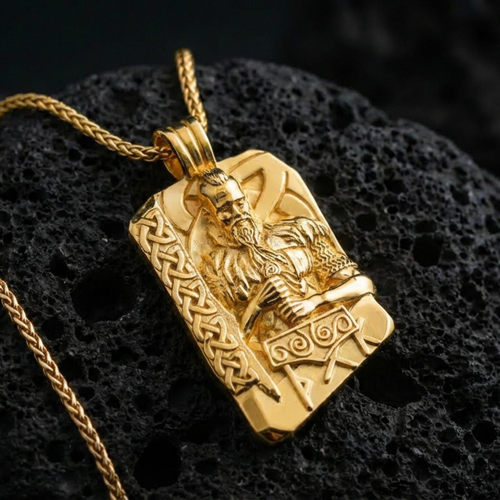 Gold plated Thor pendant necklace on textured volcanic rock, premium close-up with warm reflective shine across the warrior figure, raised runes, and detailed Mjölnir relief.