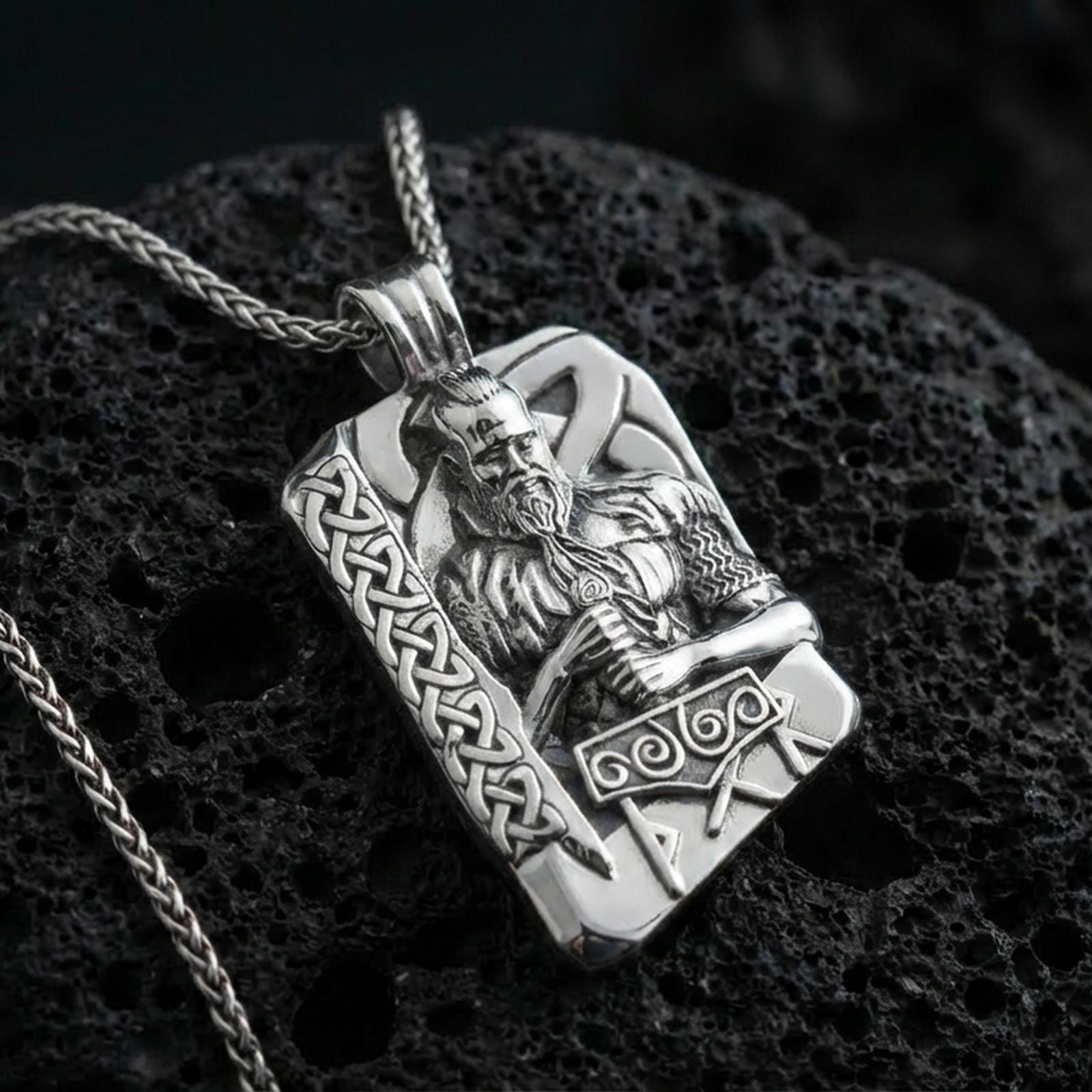 Polished silver Thor pendant necklace on textured volcanic rock, crisp macro product photo emphasizing clean edges, sharp sculpted beard detail, and bright reflective highlights on the hammer and knotwork border.
