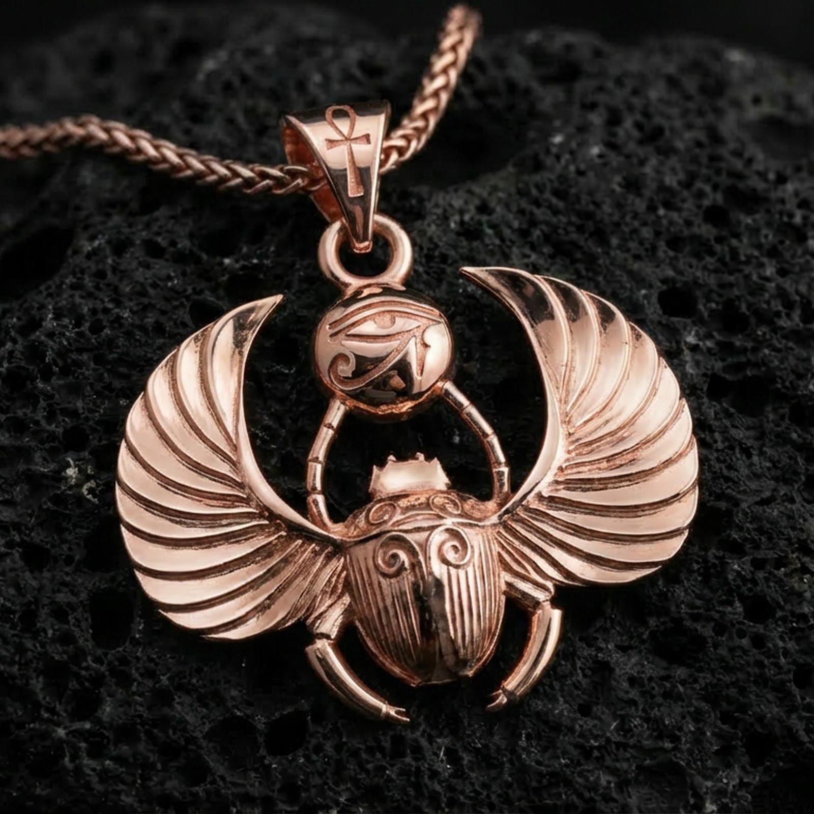 Rose gold plated winged scarab beetle pendant necklace on textured volcanic rock, centered studio-style close-up showcasing soft rosy glow and intricate Egyptian amulet detailing with crisp wing contours.
