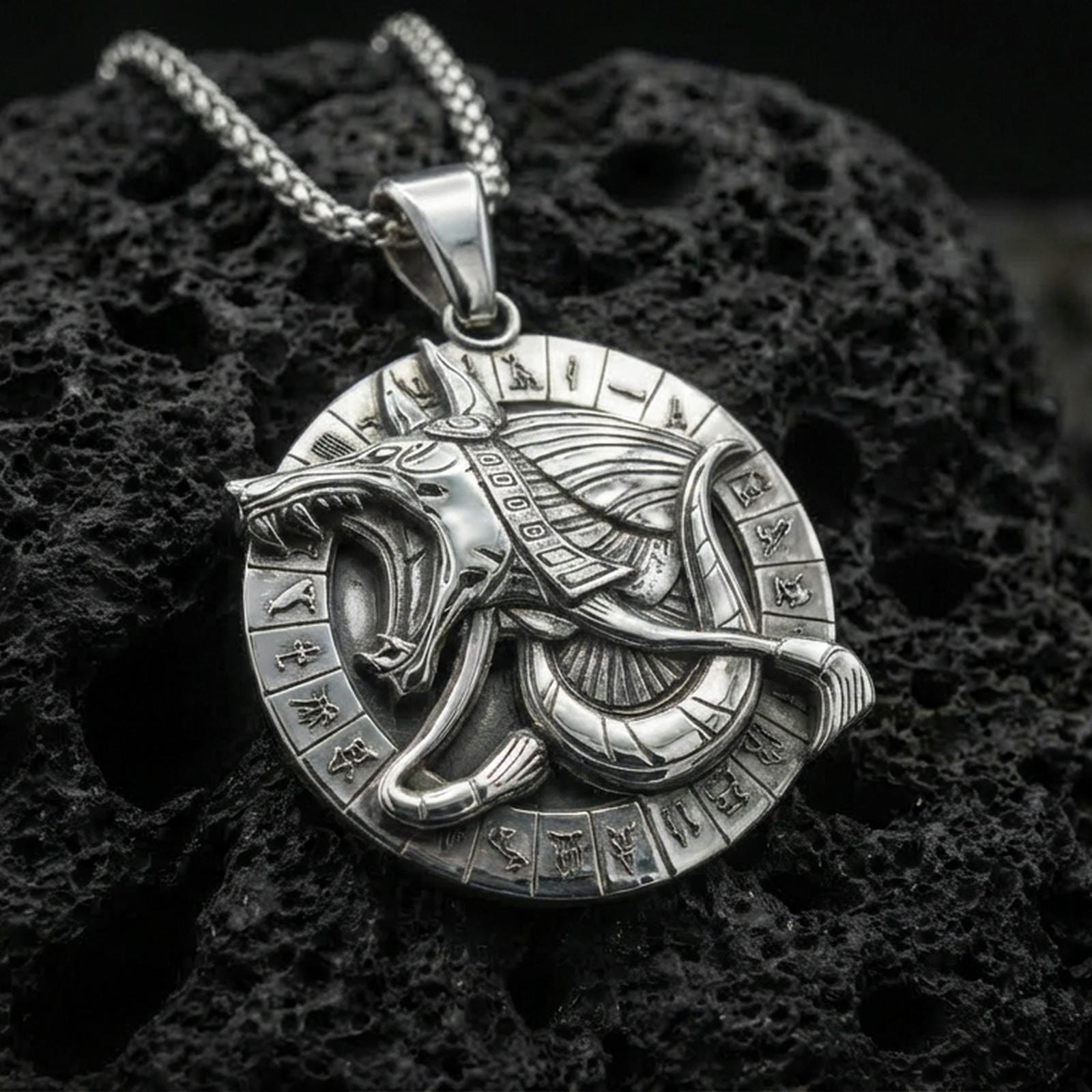 Polished silver Anubis medallion pendant necklace on textured volcanic rock, crisp macro product photo emphasizing clean edges, sharp hieroglyph symbols, and bright reflective highlights on the jackal relief.