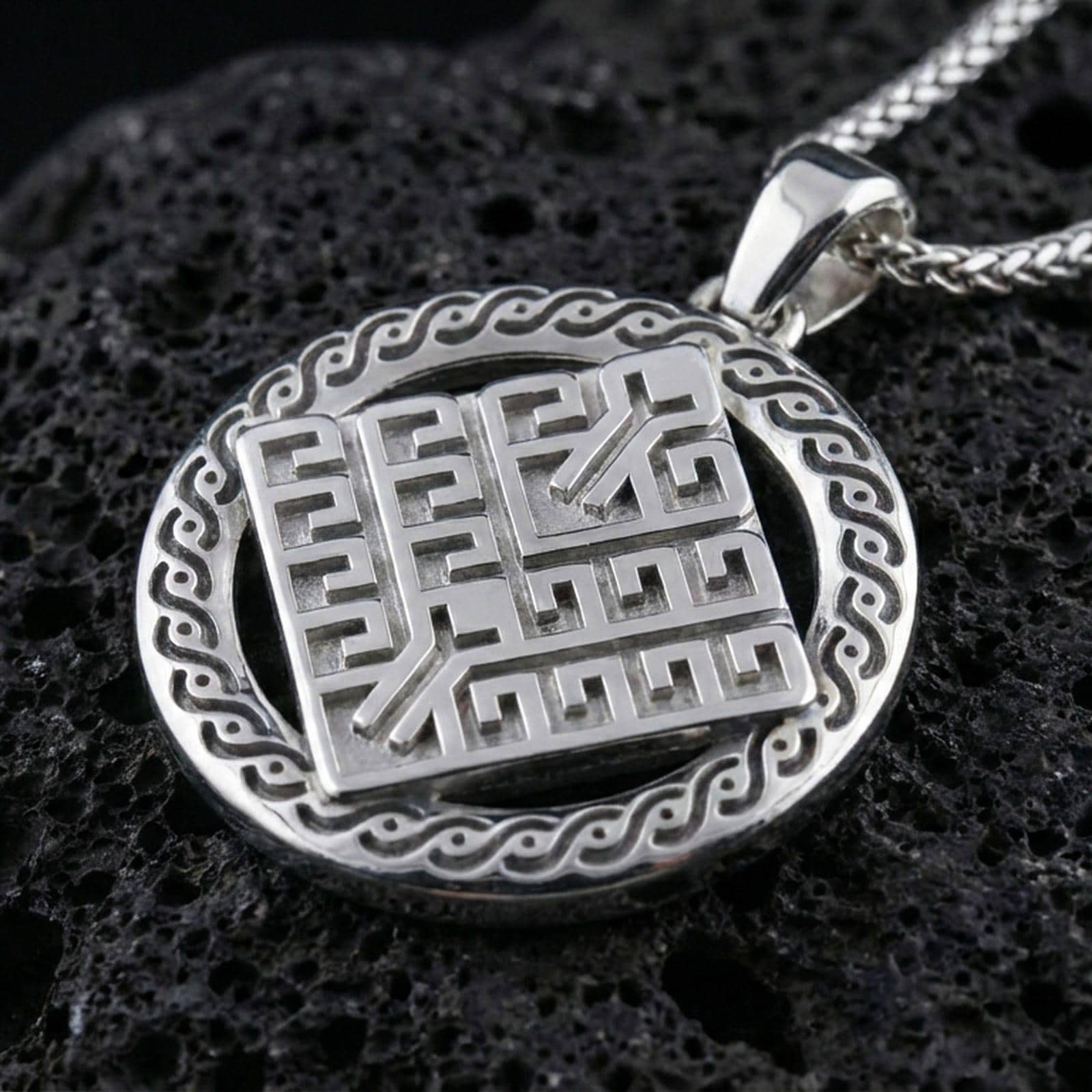 Polished silver geometric rune-style medallion pendant necklace on textured volcanic rock, crisp macro product photo emphasizing clean edges, sharp angular relief, and bright reflective highlights across the round frame.