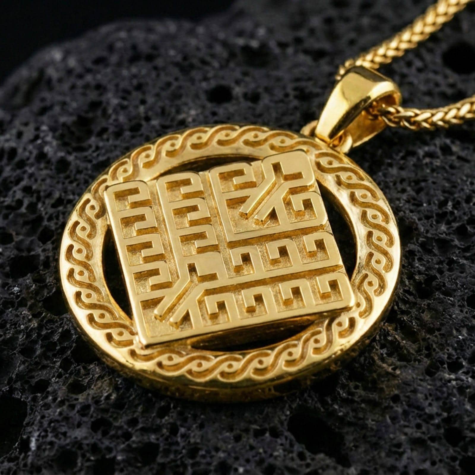 Gold plated geometric rune-style medallion pendant necklace on textured volcanic rock, premium close-up with warm reflective shine across the bold linear motif and decorative border detailing.