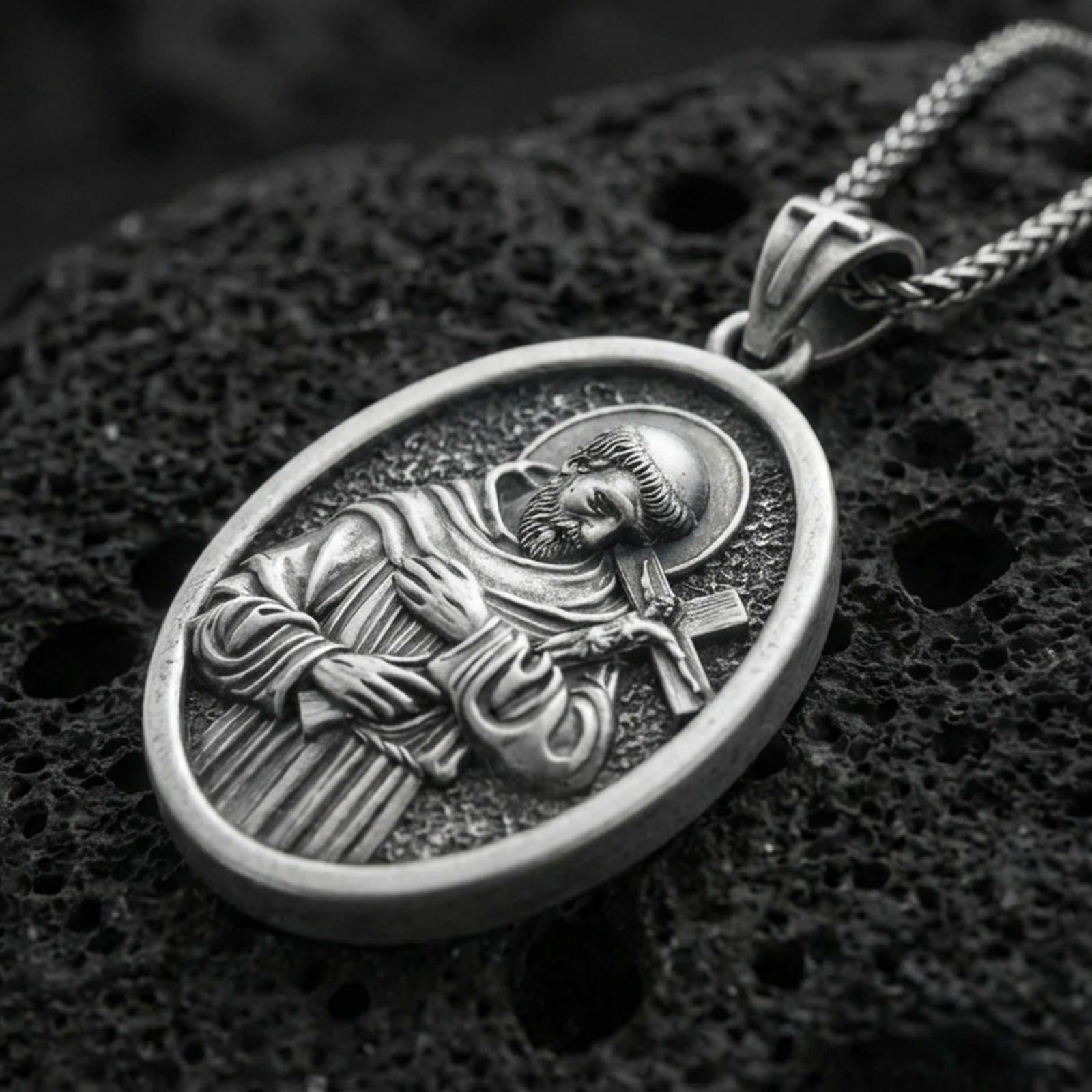 Oxidized Saint Francis pendant with halo, cross detail, and oval devotional portrait displayed on dark volcanic rock in a close-up luxury jewelry composition