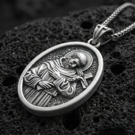 Oxidized Saint Francis pendant with halo, cross detail, and oval devotional portrait displayed on dark volcanic rock in a close-up luxury jewelry composition