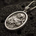 Load image into Gallery viewer, Bronze Saint Francis pendant with halo, cross detail, and oval devotional portrait displayed on dark volcanic rock in a close-up luxury jewelry composition
