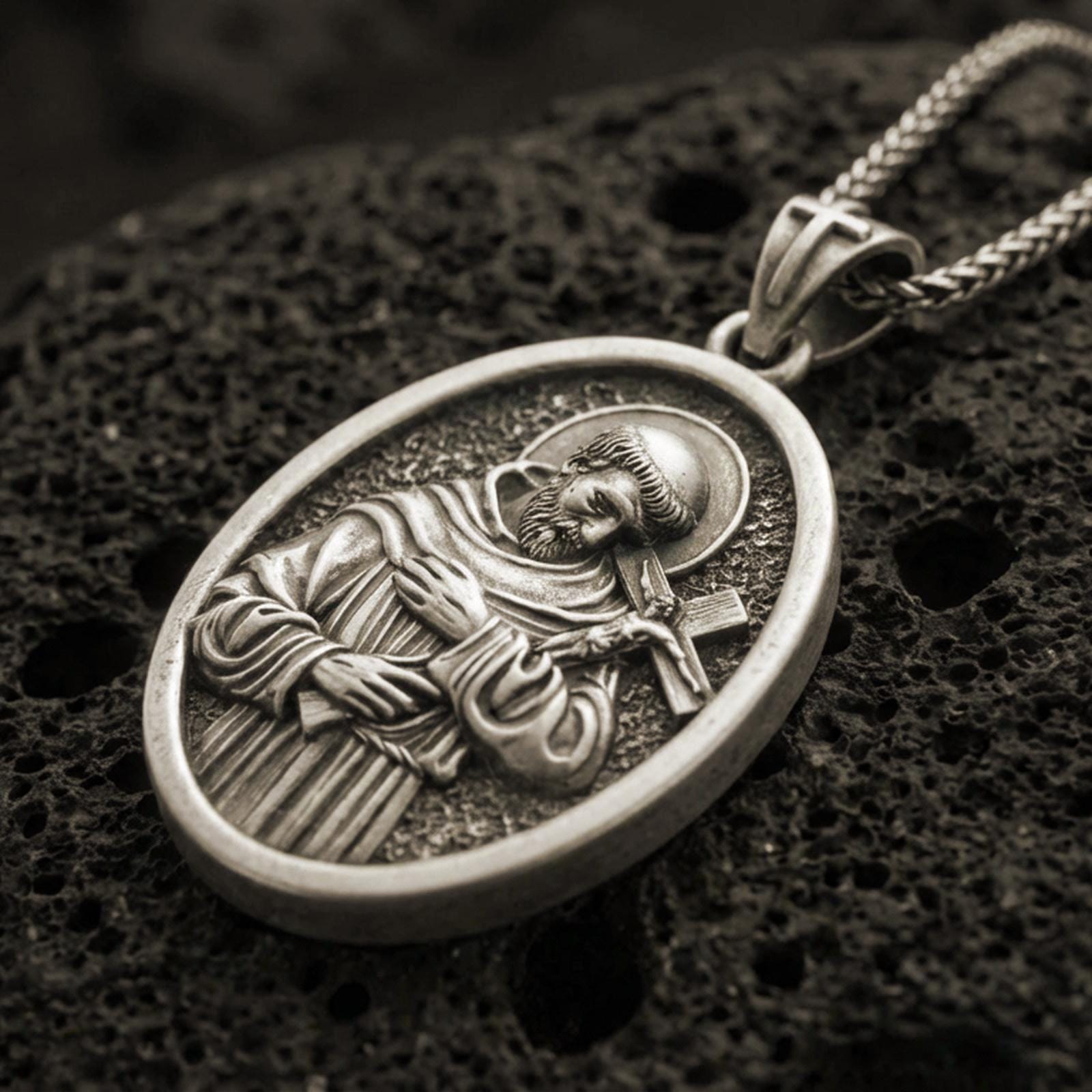 Bronze Saint Francis pendant with halo, cross detail, and oval devotional portrait displayed on dark volcanic rock in a close-up luxury jewelry composition