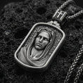 Load image into Gallery viewer, Oxidized Virgin Mary pendant with serene veiled portrait and rounded rectangular frame displayed on dark volcanic rock in a close-up luxury jewelry composition
