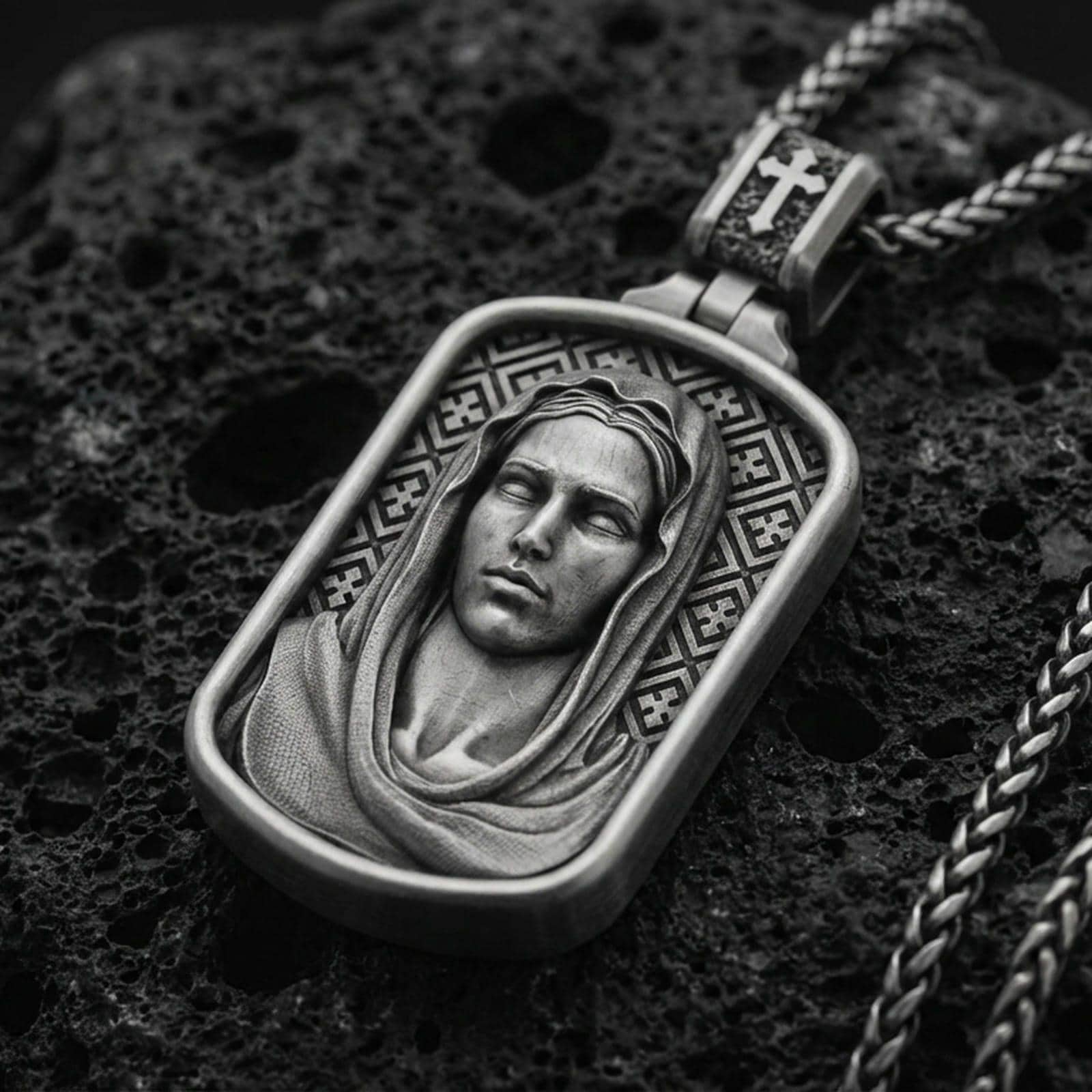 Oxidized Virgin Mary pendant with serene veiled portrait and rounded rectangular frame displayed on dark volcanic rock in a close-up luxury jewelry composition