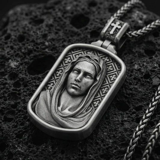 Oxidized Virgin Mary pendant with serene veiled portrait and rounded rectangular frame displayed on dark volcanic rock in a close-up luxury jewelry composition