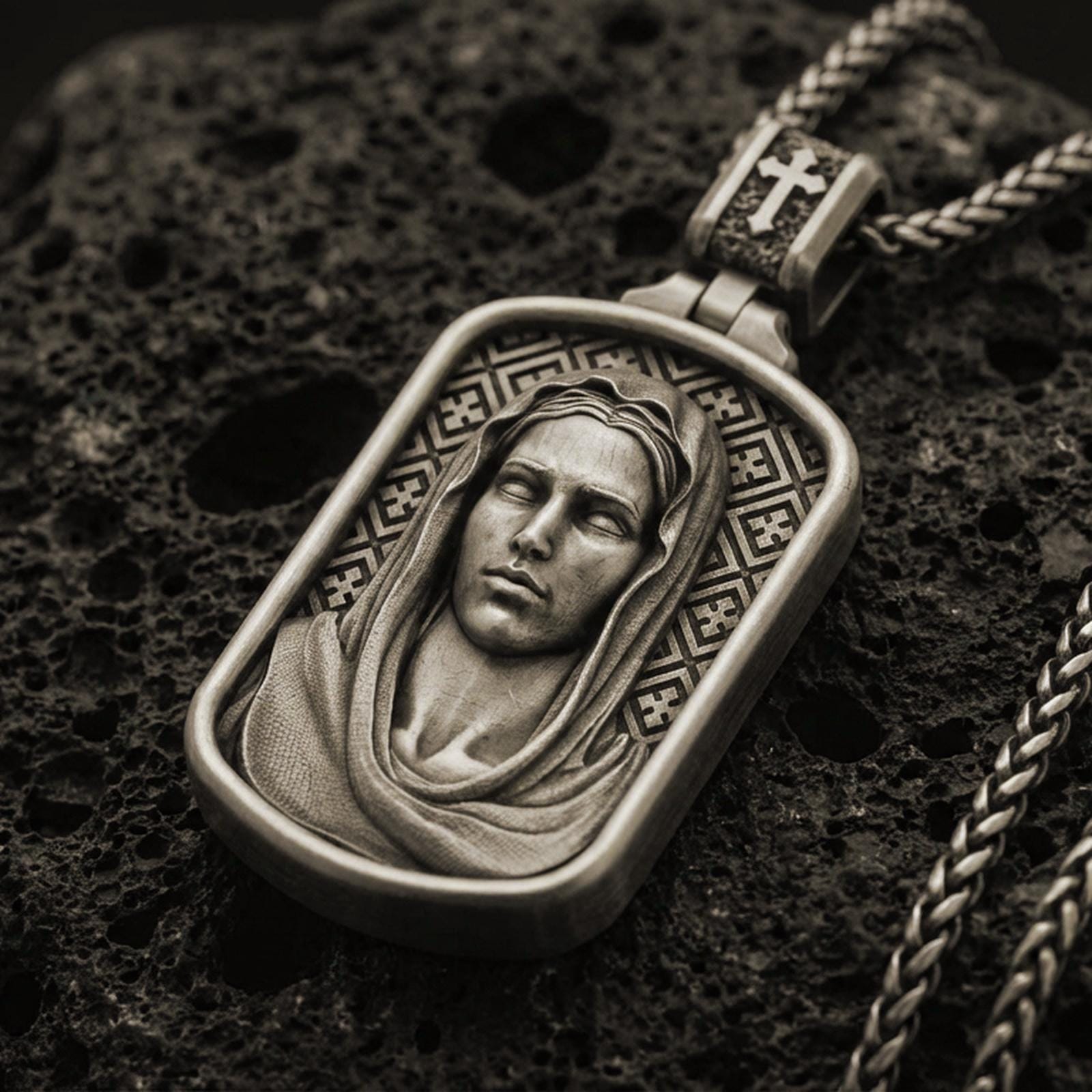 Bronze Virgin Mary pendant with serene veiled portrait and rounded rectangular frame displayed on dark volcanic rock in a close-up luxury jewelry composition