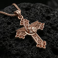 Load image into Gallery viewer, Rose gold plated Archangel Michael cross pendant with sacred warrior motif, shield emblem, and gothic-inspired scroll details resting on volcanic rock in an elegant close-up product presentation
