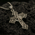 Load image into Gallery viewer, Bronze Saint Michael cross pendant with winged archangel figure, shield detail, and ornate gothic scrollwork displayed on dark volcanic rock in a close-up luxury jewelry composition
