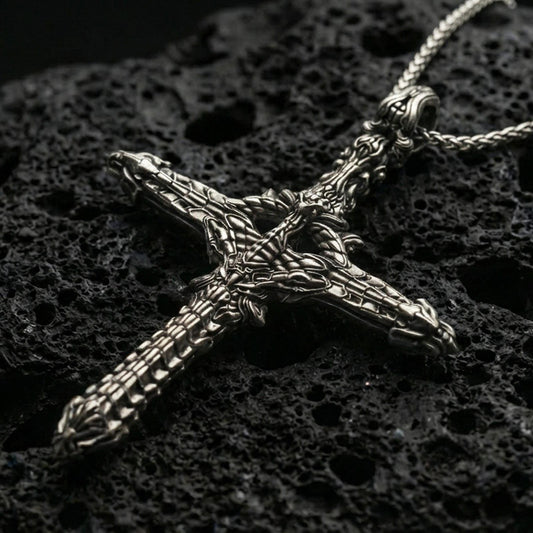 Oxidized biomechanical gothic cross pendant with intricate skeletal and machine-like detailing displayed on dark volcanic rock in a close-up luxury jewelry composition