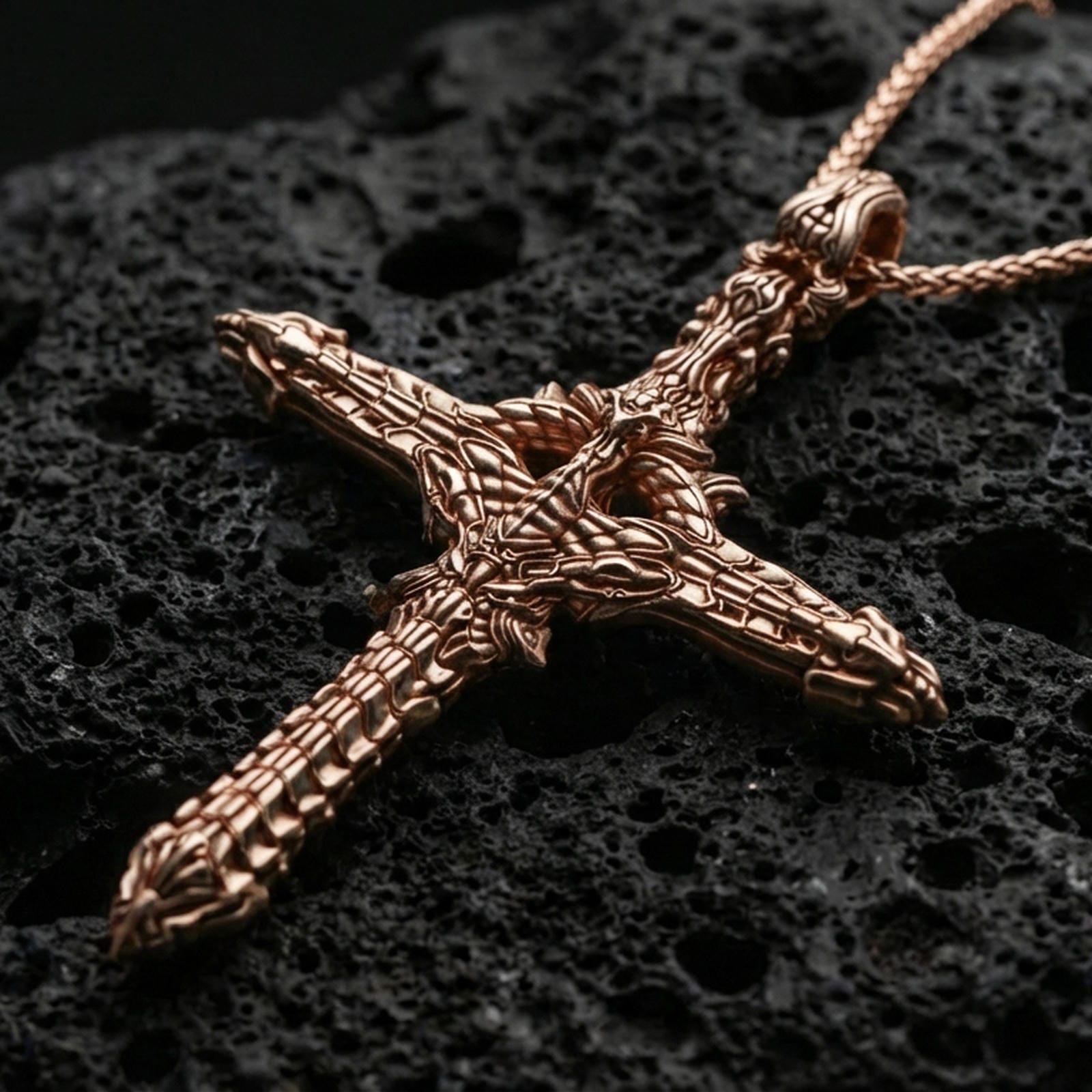 Rose gold plated gothic cross pendant with intricate biomechanical design, sculpted industrial-organic relief, and dramatic elongated form resting on volcanic rock in an elegant close-up product presentation
