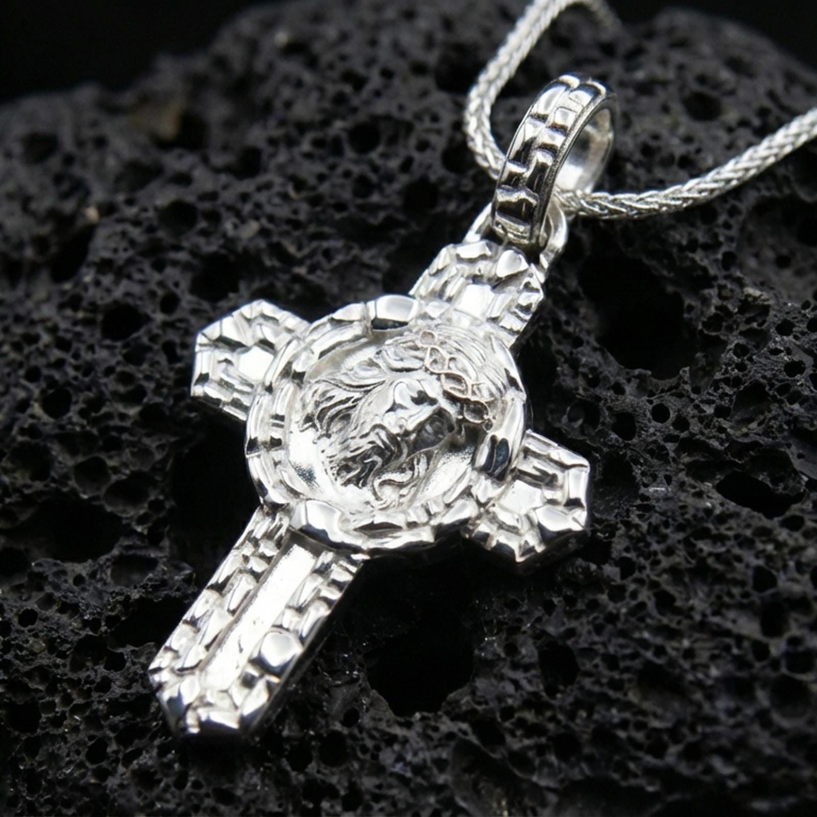 Polished 925 sterling silver Christ crucifix necklace on black volcanic stone with detailed cross texture.