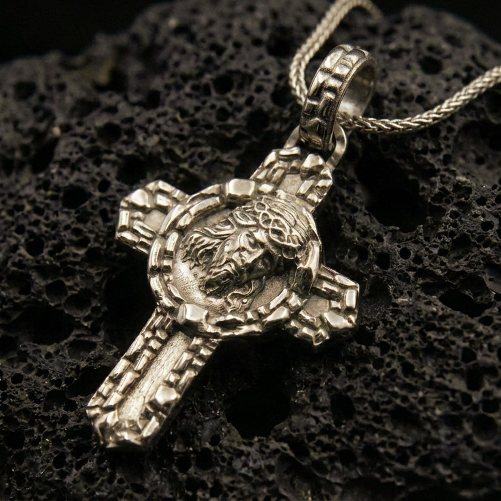 Bronze Jesus crucifix pendant on black volcanic rock with crown of thorns relief.