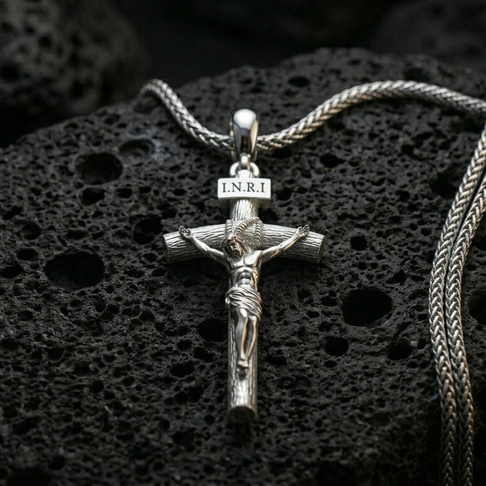 Polished silver Jesus crucifix necklace with detailed corpus relief, INRI plaque, and classic cross silhouette placed on textured volcanic rock in a premium studio product shot