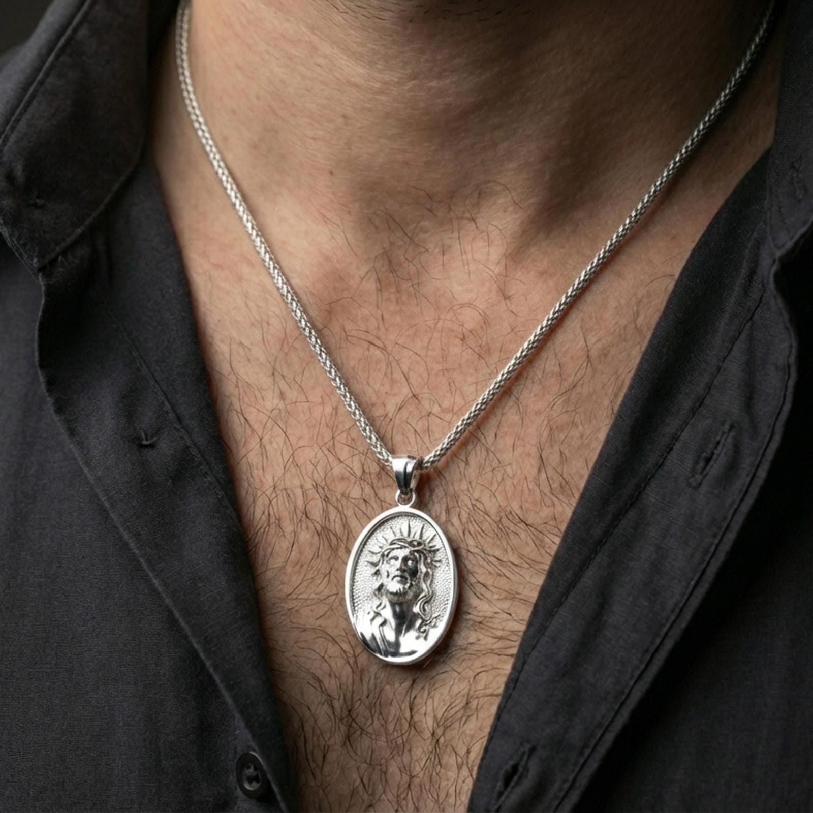 Polished silver Jesus medal with sacred portrait and crown of thorns worn on the neck in a close lifestyle frame, highlighting the refined facial relief and oval design