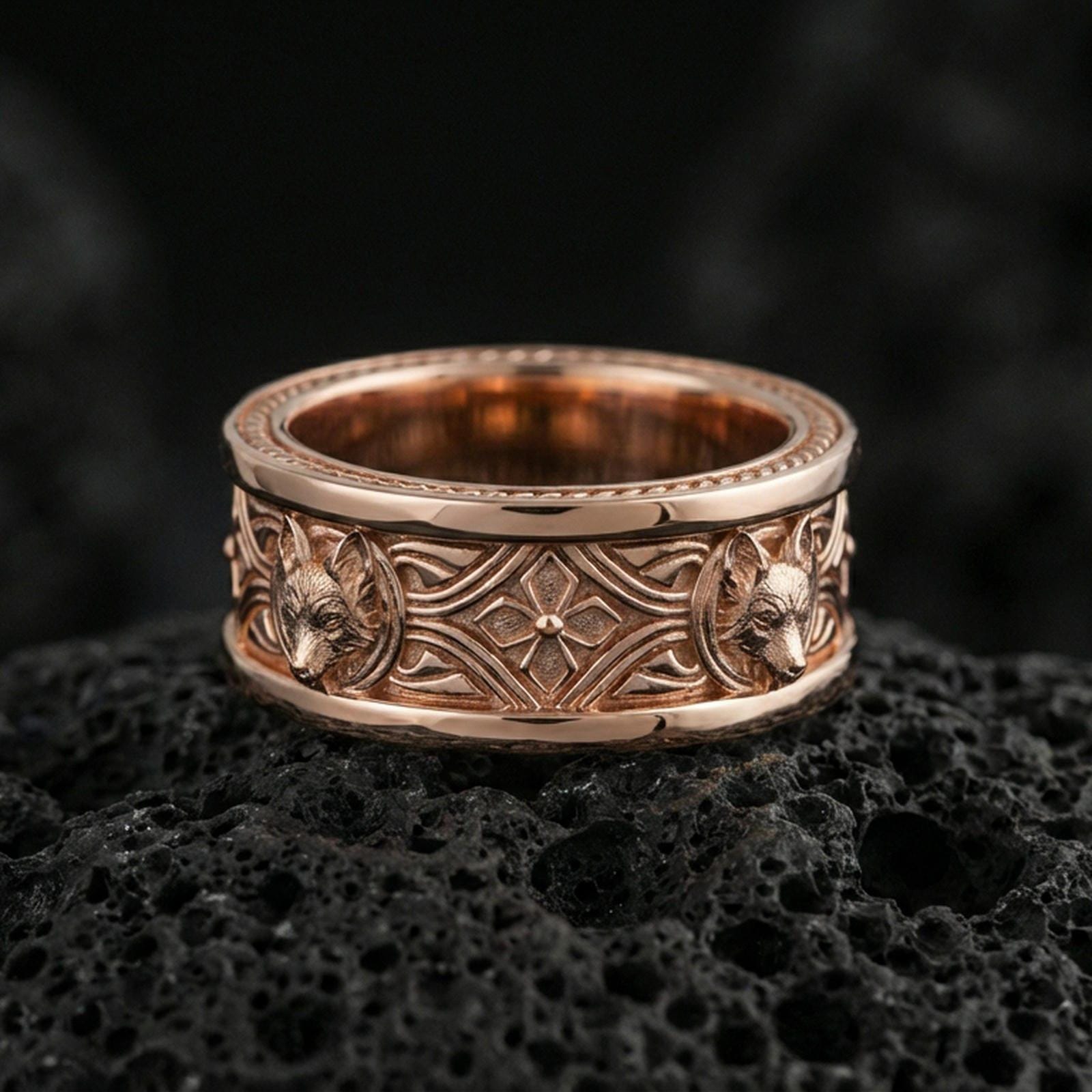 Rose gold plated fox band ring on textured volcanic rock, centered studio-style close-up showcasing soft rosy glow and intricate fox-and-scroll detailing with a refined finish.