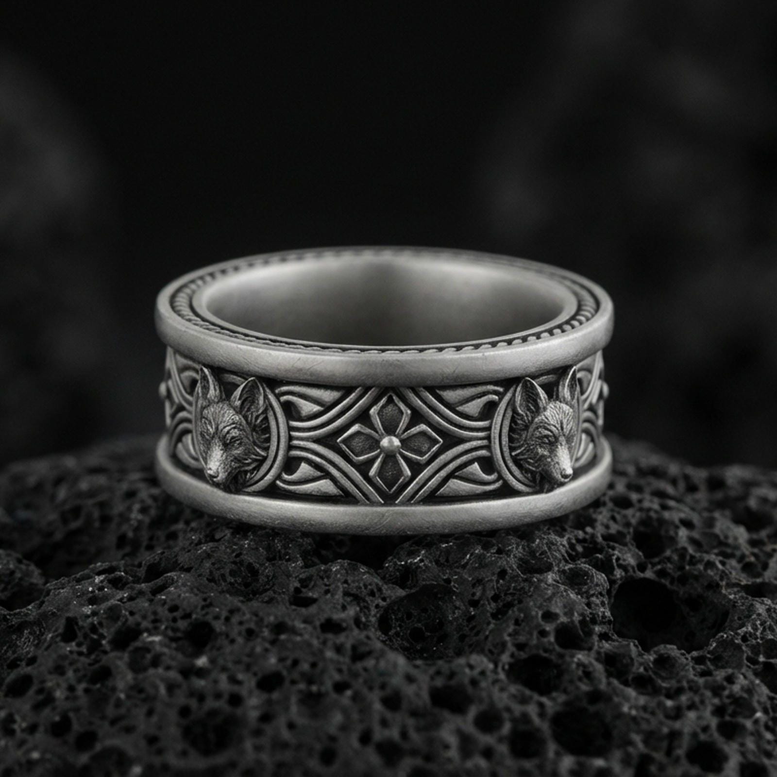 Oxidized fox band ring on textured volcanic rock, centered close-up highlighting the carved fox heads, ornate scrollwork, and deep antique shadowed contrast.