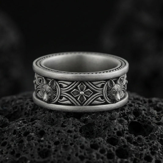 Oxidized fox band ring on textured volcanic rock, centered close-up highlighting the carved fox heads, ornate scrollwork, and deep antique shadowed contrast.