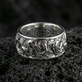 Load image into Gallery viewer, Polished silver koi fish band ring on textured volcanic rock, crisp macro product photo emphasizing clean edges, sharp engraved scales, and bright reflective highlights across the patterned band.
