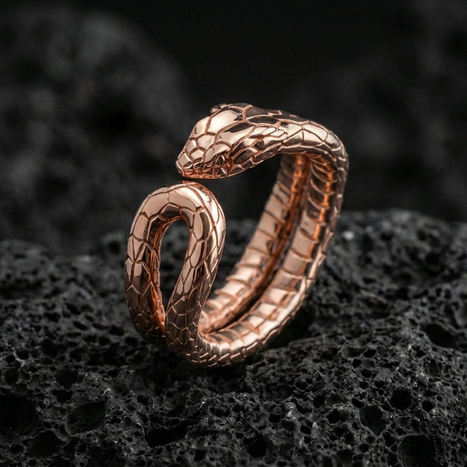 Rose gold plated snake wrap ring on textured volcanic rock, centered studio-style close-up showcasing soft rosy glow and refined serpent silhouette with crisp scale detailing.