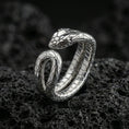 Load image into Gallery viewer, Polished silver snake wrap ring on textured volcanic rock, crisp macro product photo emphasizing clean edges, sharp scale engraving, and bright reflective highlights on the serpent head.
