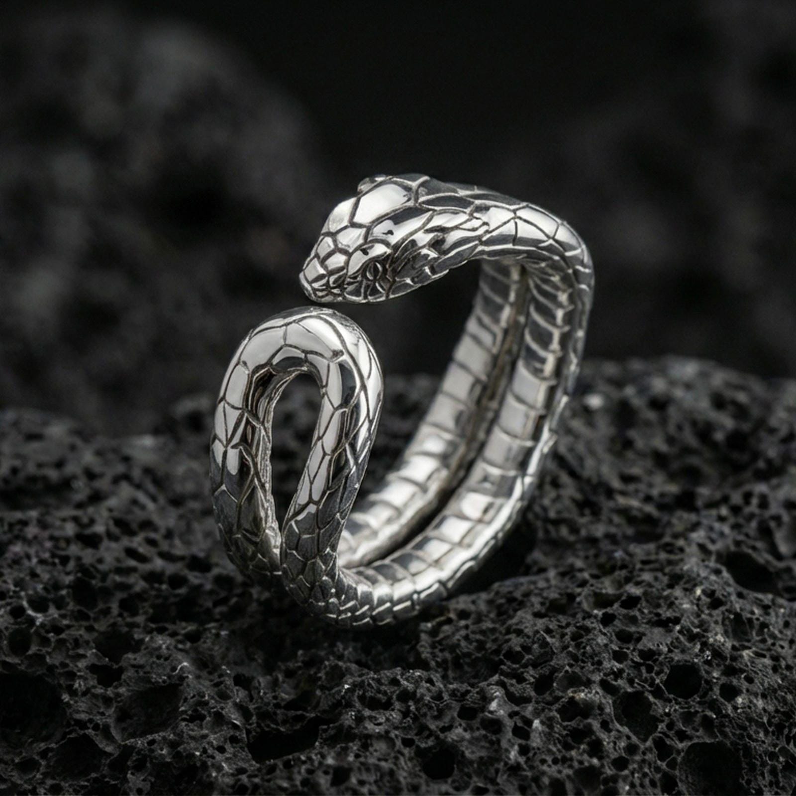 Polished silver snake wrap ring on textured volcanic rock, crisp macro product photo emphasizing clean edges, sharp scale engraving, and bright reflective highlights on the serpent head.