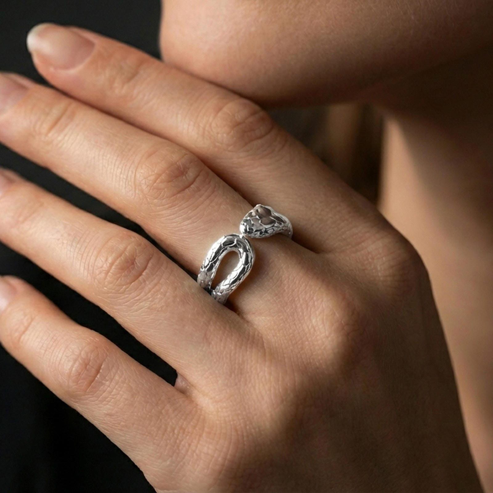 Polished silver snake wrap ring worn on a finger, clean lifestyle wear shot capturing bright shine and the detailed serpent head-and-scale relief in natural light.