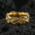 Load image into Gallery viewer, Gold plated floral band ring on textured volcanic rock, premium close-up with warm reflective shine across the lily shapes, sculpted petals, and raised ornamental contours.
