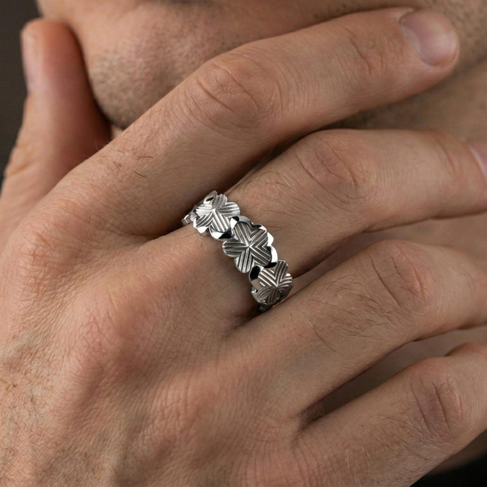 Polished silver floral band ring worn on a finger, clean lifestyle wear shot capturing bright shine and the detailed lily relief in natural light.